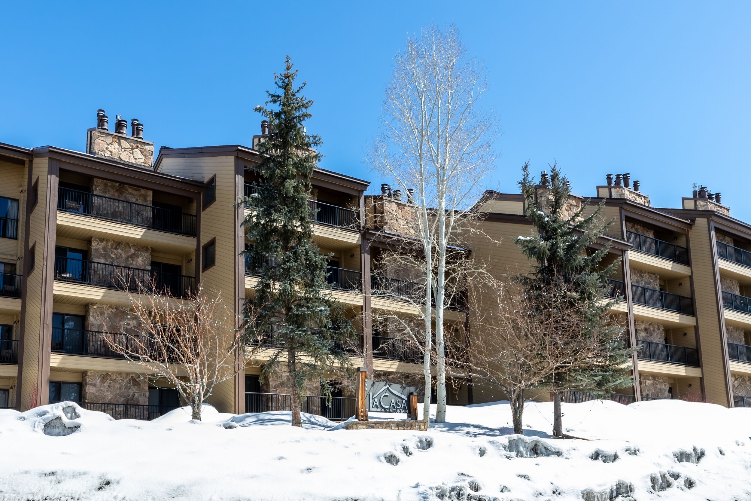 A multi-story building with balconies, a snow-covered ground, and a clear blue sky.