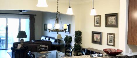 A modern kitchen with granite countertops, stainless steel sink, pendant lighting, and a dining area with a sofa and chairs.