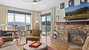 A spacious living room with a fireplace, comfortable seating, a television, and a scenic view through large windows. - Walk to Downtown, Top Floor- Seasons at Sandpoint (Sandpoint)