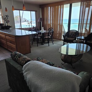 A spacious living area with a dining table, chairs, a sofa, and a balcony with a view of the sea.