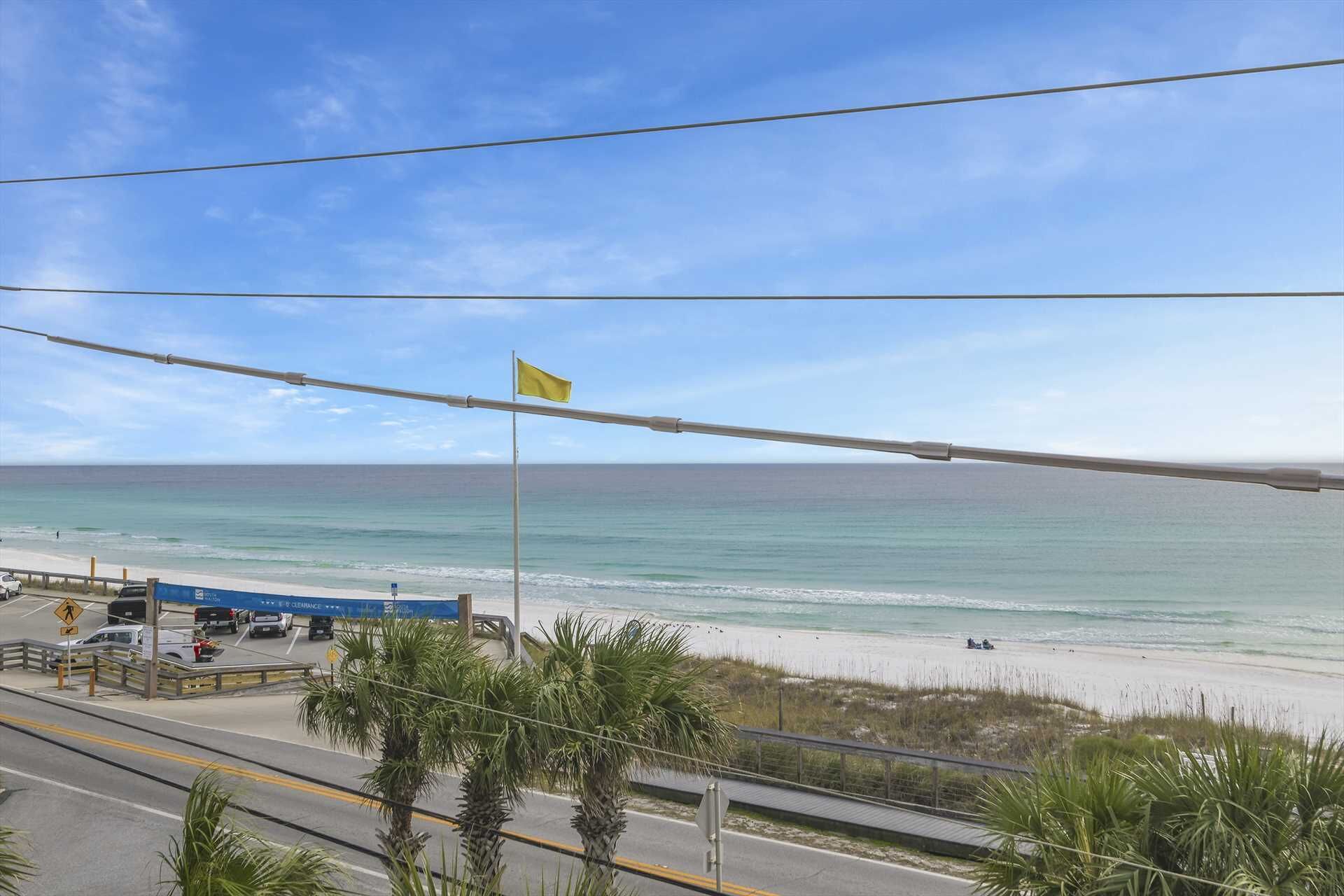 A coastal road with a beach view, palm trees, and a flag on a pole.