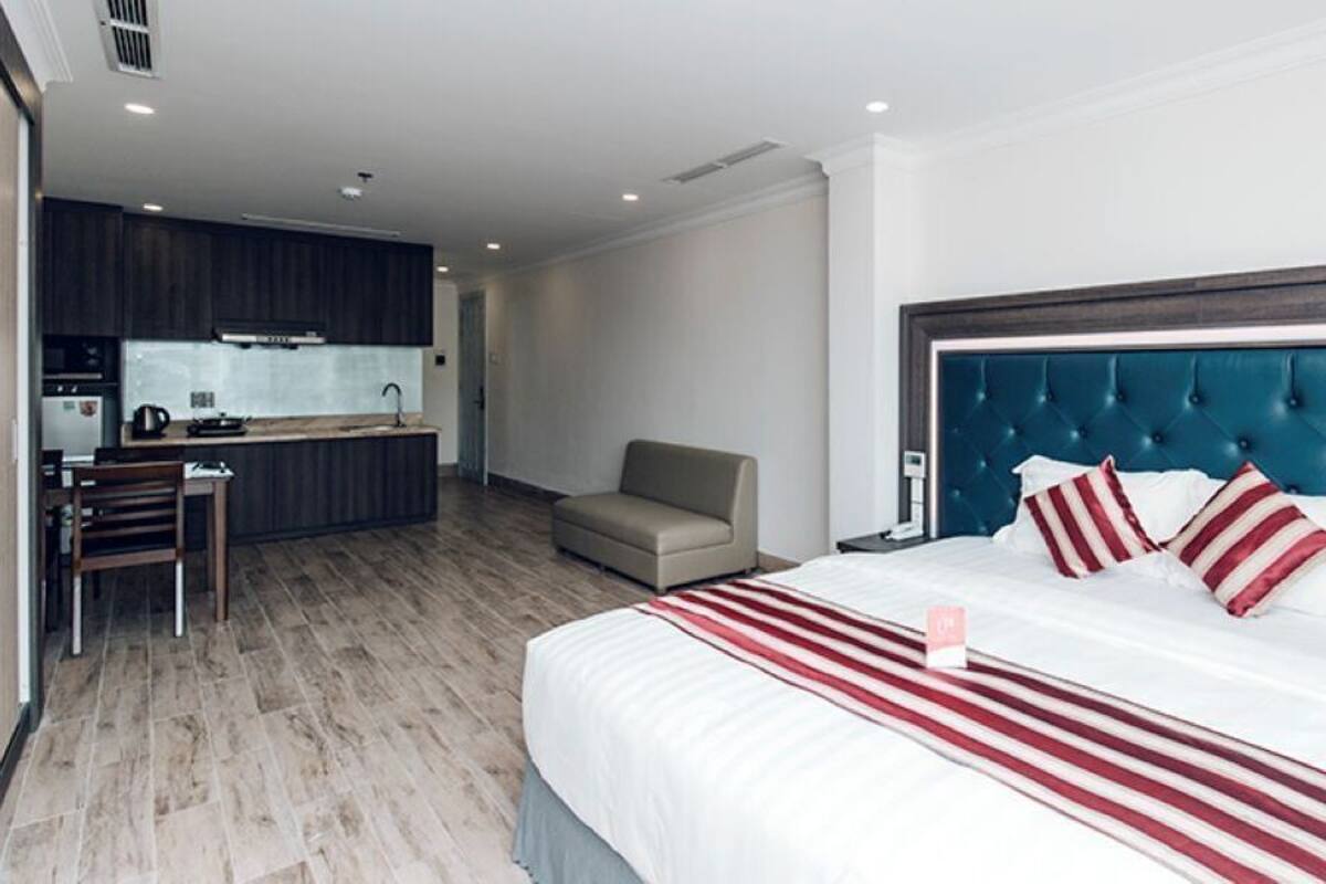 A hotel room with a large bed, a blue headboard, a kitchenette, and a seating area.