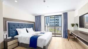 A hotel room with a large bed, a desk, and a balcony with a view of buildings. - Seven Seas Hotel and Apartment (Nha Trang)