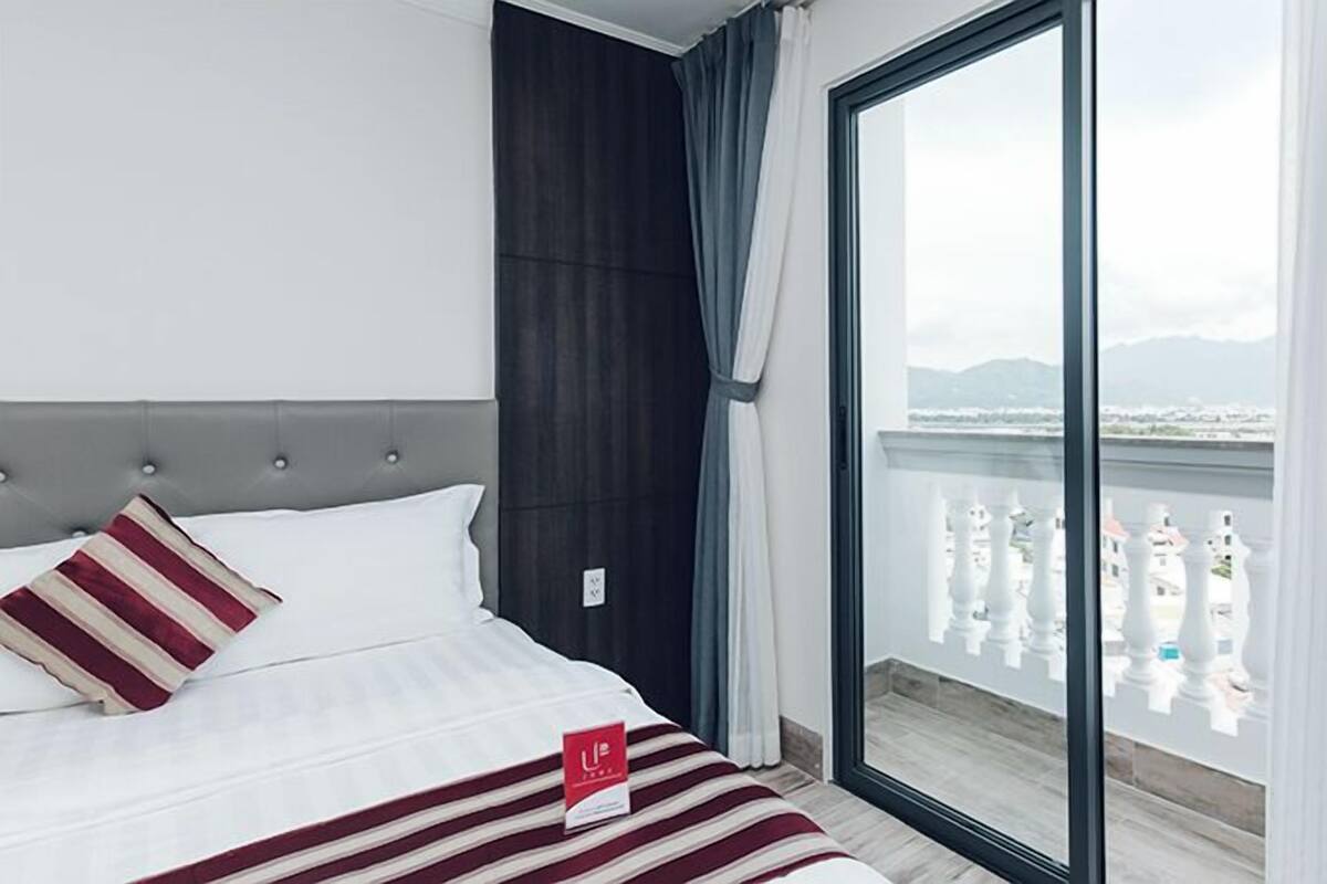 A hotel room with a large bed, a dark headboard, and a view of a balcony with white balustrades.