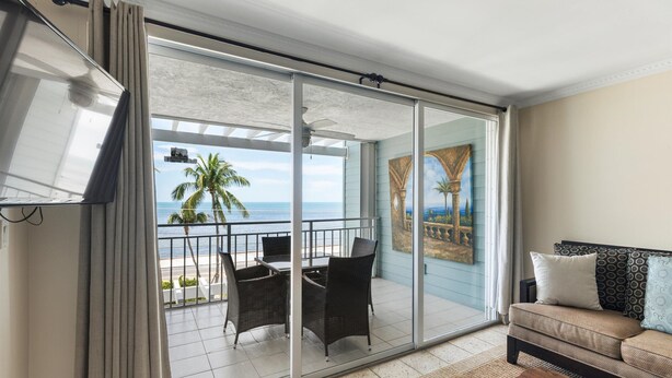 A balcony with a view of the ocean, a dining table with chairs, and a sofa with cushions. - Direct Ocean View from Your Condo-No Contact Check-In (Key West)