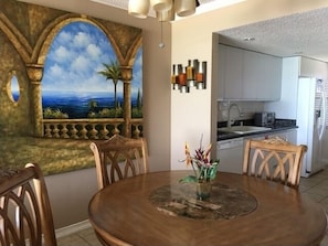 Enjoy meals in this dining area with a round table and comfortable seating, surrounded by a beautiful coastal landscape painting.
