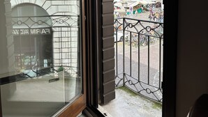 Blick aus einem Fenster eines Gebäudes mit steinverkleideter Fassade, ein Balkon mit Metallgeländern und ein Innenhof mit Personen und Fahrrädern.