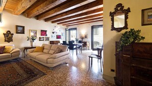 Ein geräumiges Wohnzimmer mit hoher Holzbalkendecke, einem großen beigen Sofa, einem Essbereich mit Tisch und Stühlen sowie einem Holzschrank.