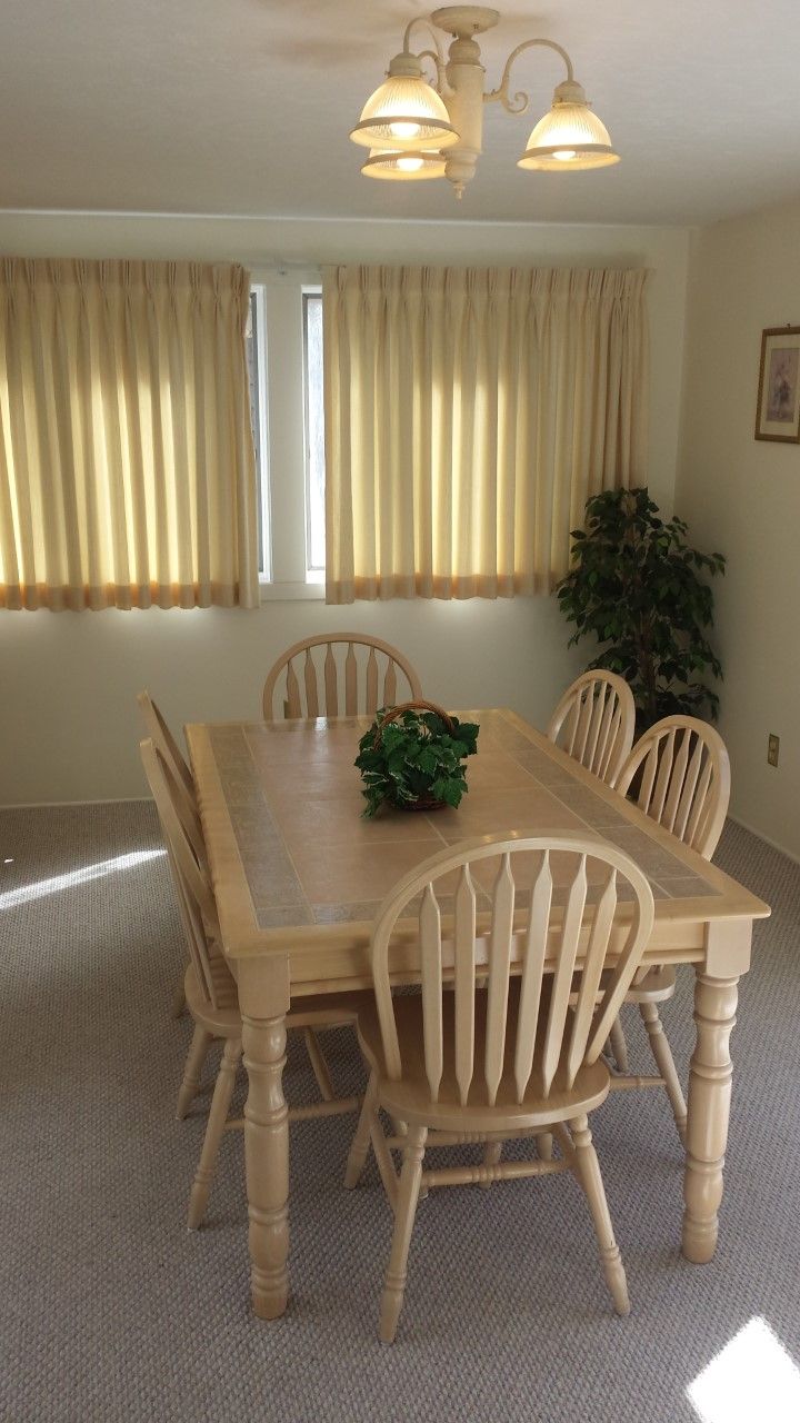 A dining room with a wooden table and chairs, a chandelier, and a plant.