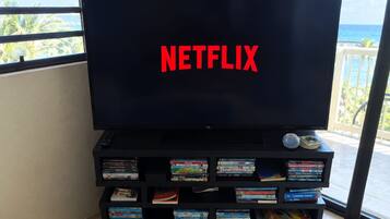 A television with the Netflix logo on the screen, placed on a black entertainment unit with a view of the ocean through a window.