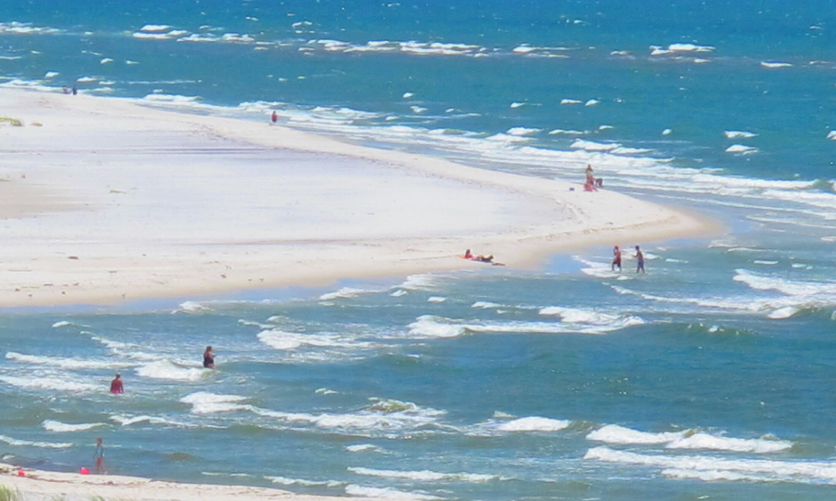 A beach with people swimming and walking along the shore.