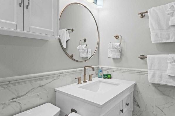 Un baño moderno con tocador de mármol, un espejo grande y varios ganchos para toallas.