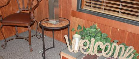 A wooden chair, a small table with a vase, and a welcome sign with rope letters.