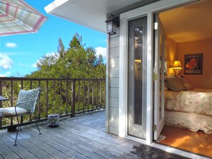 A balcony with a chair and a decorative pot, a sliding glass door to a bedroom with a bed and a lamp, and a view of trees and sky.