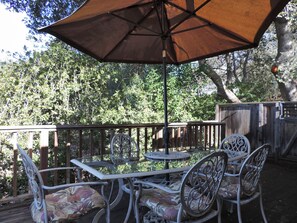 An outdoor patio with a table and chairs, a large umbrella, and a wooden deck.