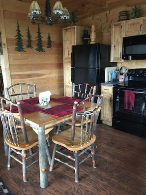 Una mesa de comedor de madera rústica con cuatro sillas, un refrigerador negro, un microondas y una estufa en una cocina de estilo cabaña.