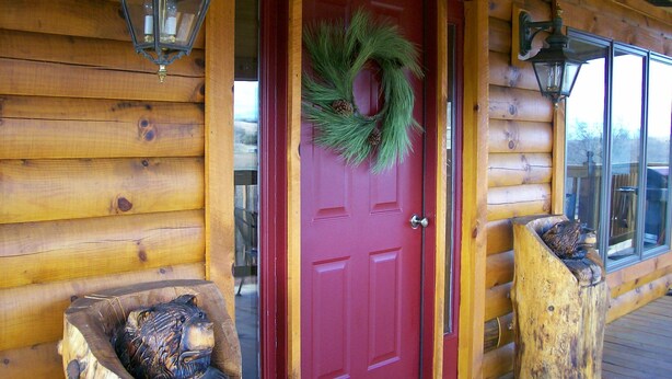 Een houten chalet met een rode deur, twee houten banken en een krans op de deur.