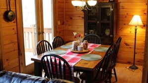 A wooden dining room with a table set for four, chairs, a chandelier, and a lamp. - Creek Front Mountain Cabin with Jacuzzi. (Andrews)