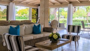 A spacious indoor area with a high ceiling, a large sofa with blue cushions, striped chairs, and a coffee table.