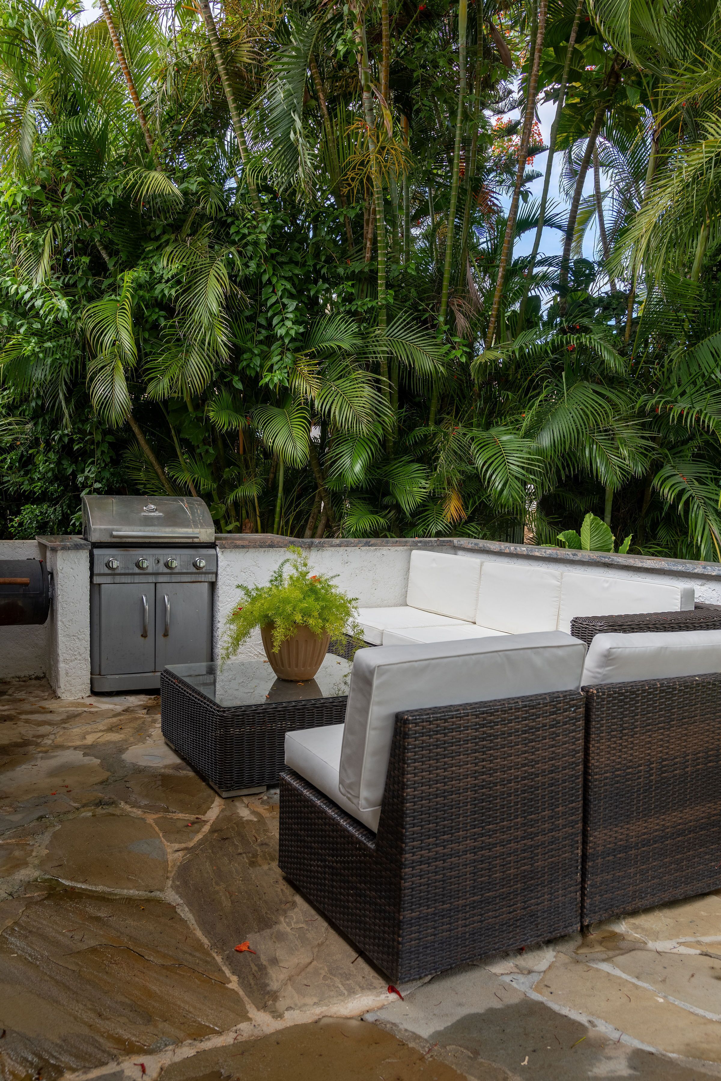 Un patio al aire libre con una parrilla, muebles de mimbre y suelo de piedra.