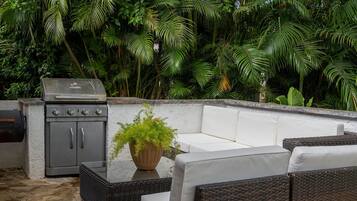 Un patio al aire libre con una parrilla, muebles de mimbre y suelo de piedra.