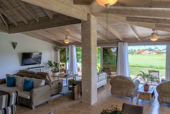A spacious living area with a high ceiling, comfortable seating, a flat-screen TV, and large windows offering a view of a green landscape. - The view isn't just a feature—it’s the backdrop to every memory you’ll make! (La Romana)