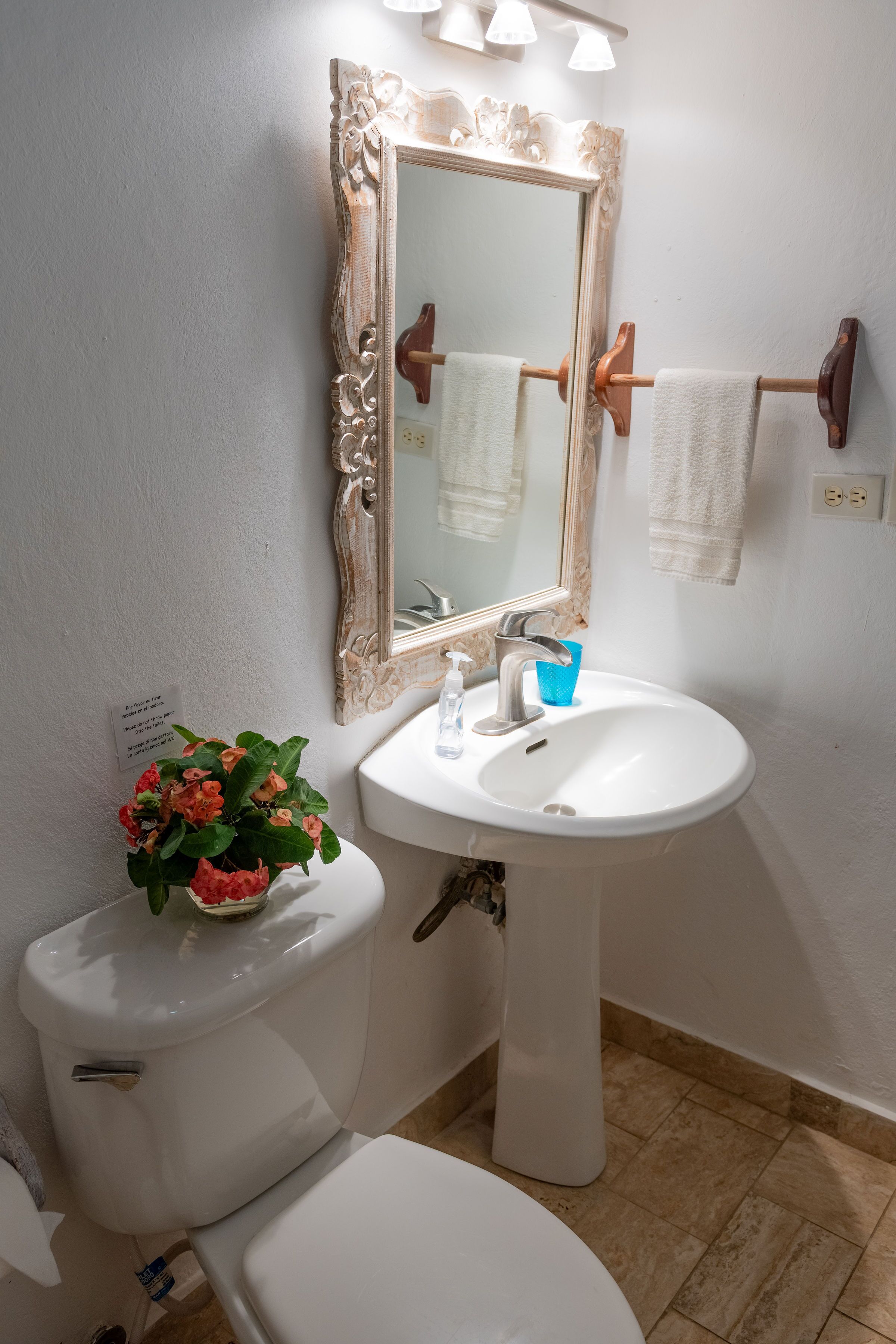 Un baño con inodoro y lavamanos blancos, y un espejo con marco decorativo.