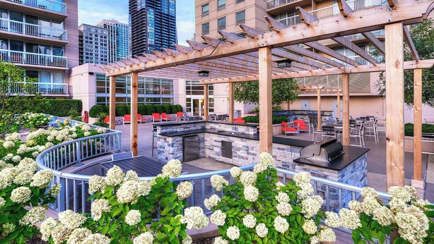 Un espace extérieur aménagé en terrasse, avec un barbecue en pierre et des sièges, le tout entouré de buissons d’hortensias blancs.