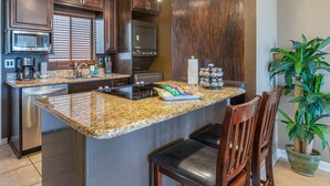 Eine Küche mit Granit-Arbeitsplatten, Edelstahlgeräten, Holzschränken und einer zentralen Kochinsel mit Barhocker.