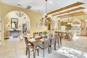 A spacious dining area with a high ceiling and exposed wooden beams, a kitchen with modern appliances, and a staircase leading to an upper level.