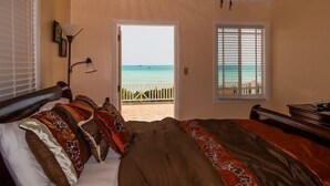 A bedroom with a bed, a ceiling fan, a window with a view of the ocean, and a door leading outside.