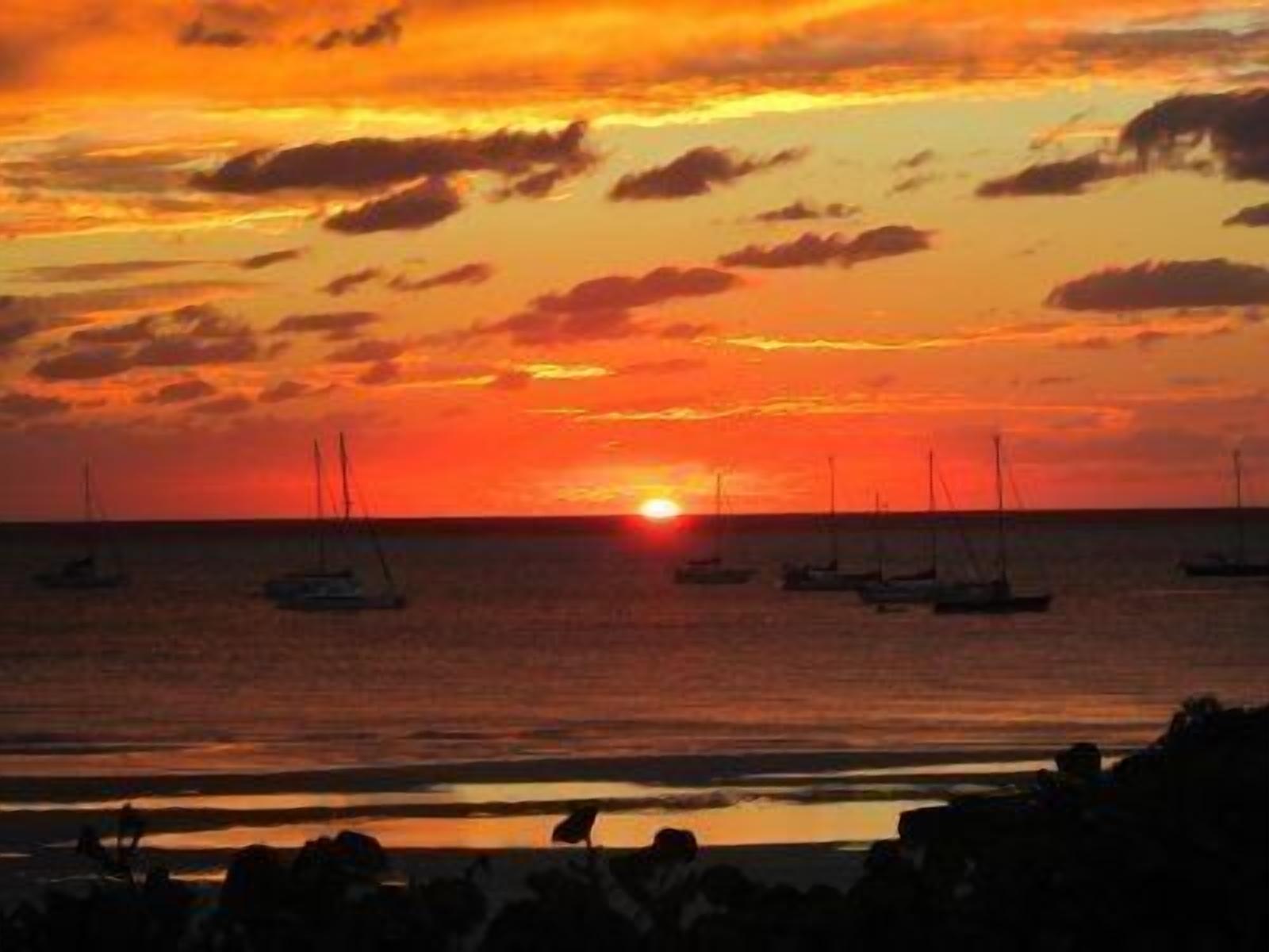 Un coucher de soleil sur une mer calme, avec plusieurs voiliers ancrés.