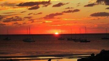 Un coucher de soleil sur une mer calme, avec plusieurs voiliers ancrés.