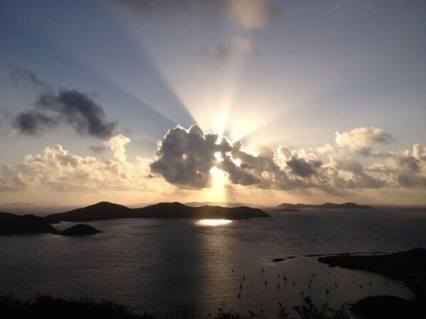 Un coucher de soleil sur une mer calme, avec des reliefs terrestres visibles au loin.