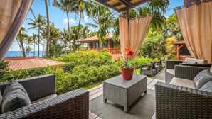 An outdoor seating area with wicker furniture, a potted plant, and a view of the ocean and palm trees.