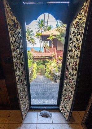A doorway leading to a tropical outdoor area with a wooden deck, palm trees, and a view of the ocean.