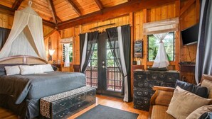 A wooden cabin bedroom with a bed, bench, dresser, and a television.