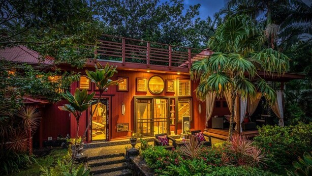 A house with a red exterior, a wooden deck, and a staircase leading to a covered porch.