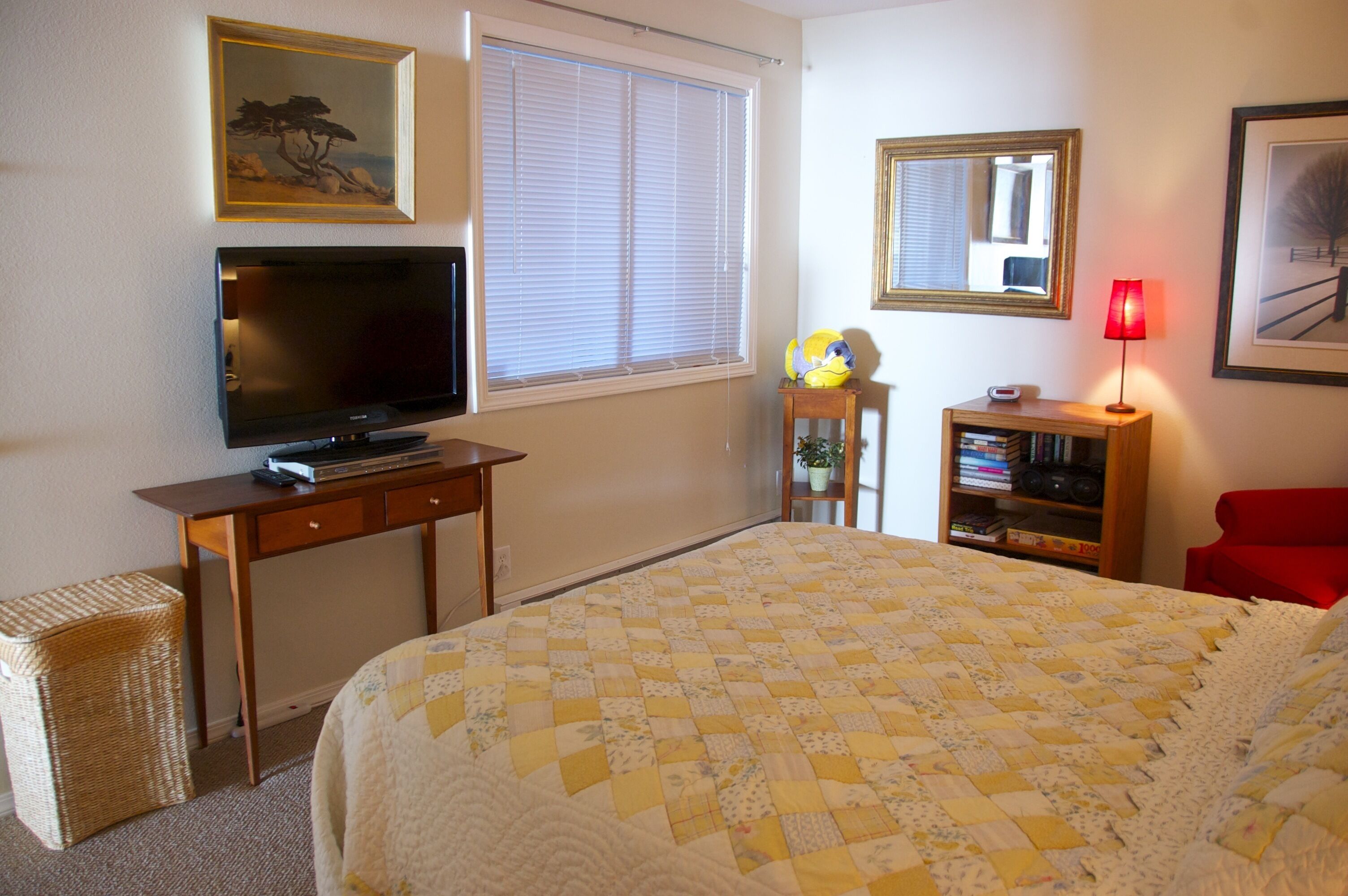 A hotel room with a bed, a television, a bookshelf, a red chair, and a window with blinds.