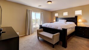 Un dormitorio con cama, mesitas de noche, un escritorio, un banco y una ventana con cortinas.