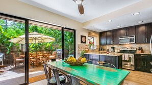 Een moderne keuken met donkere kastjes, een groen aanrecht en een eethoek met een tafel en stoelen.
