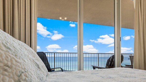 A hotel room with a large bed, a view of the ocean, and a balcony with chairs.
