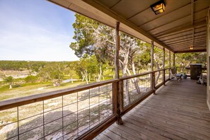 Un espacio al aire libre techado con piso de madera, barandilla de metal y vista a un paisaje natural con árboles y una masa de agua.
