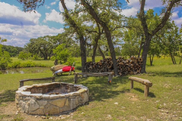 Un hogar de piedra rodeado por un banco de madera rústica y un montón de leña en un entorno exterior tranquilo.