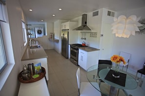 A modern kitchen with stainless steel appliances, a glass dining table, and a hanging light fixture.