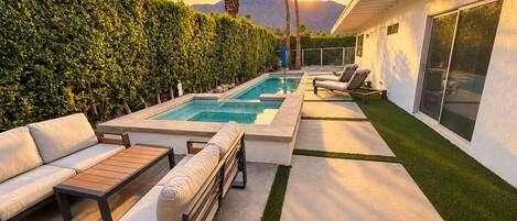 A modern outdoor pool area with a lounge, seating, and a view of mountains.