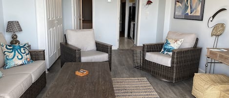 Un soggiorno con mobili in vimini, una ventola a soffitto e un quadro astratto incorniciato.