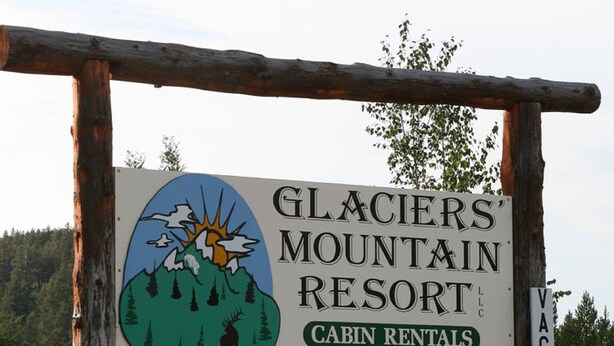 En skylt för Glaciers Mountain Resort, med information om uthyrning av stugor, kontaktnummer och adress i Coram, Montana.