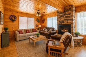 L’intérieur d’un chalet chaleureux, avec une cheminée en pierre, des murs en bois et un ventilateur de plafond.