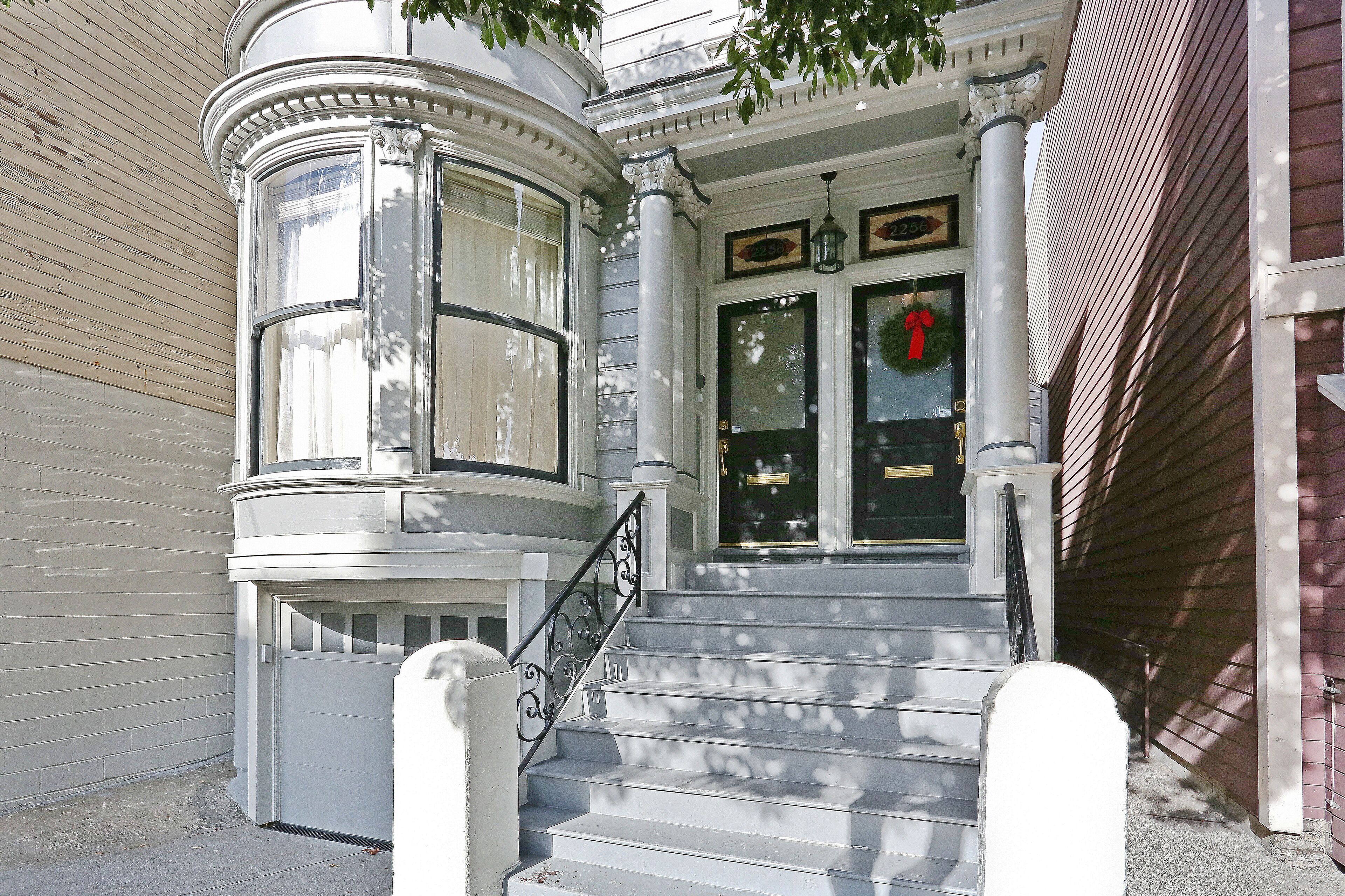 A corner building with a bay window, a set of stairs leading to a door with a wreath, and a number plaque above the door.